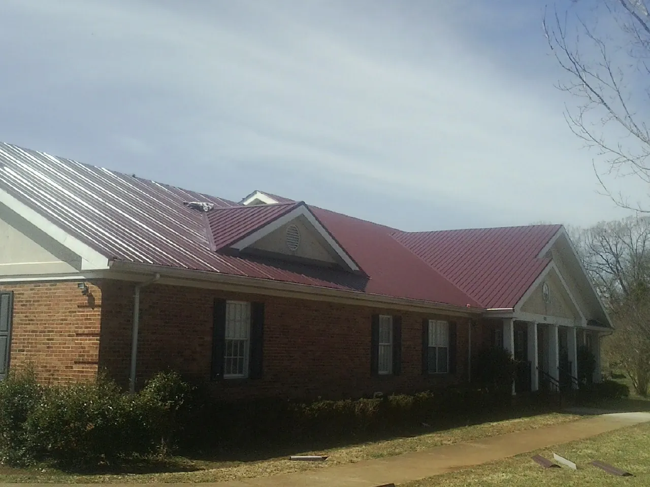 Red metal roof with gabled entries on a long brick building, from a Hail Damage Roof Repair job in Winlock