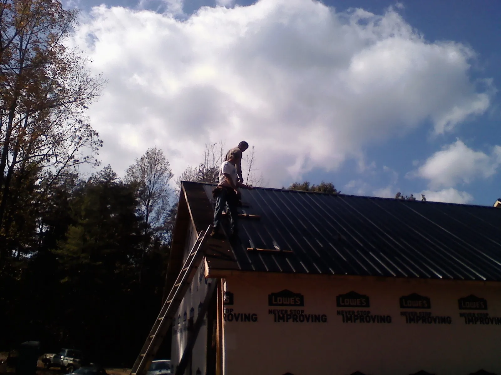 Roofer fastening dark metal panels high against a cloudy sky, from a Roof Inspection job in Winlock